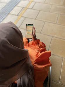 Person wearing an orange top and a headscarf, holding a smartphone displaying an app screen.