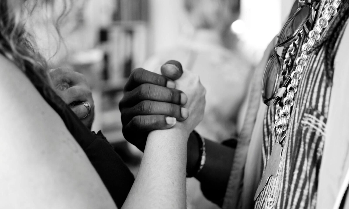 A zoomed-in black and white photograph of a black and white woman holding hands