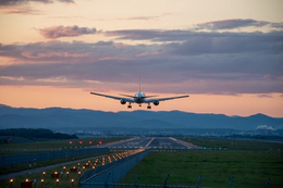 Photo of a plane above a runway at sunset.