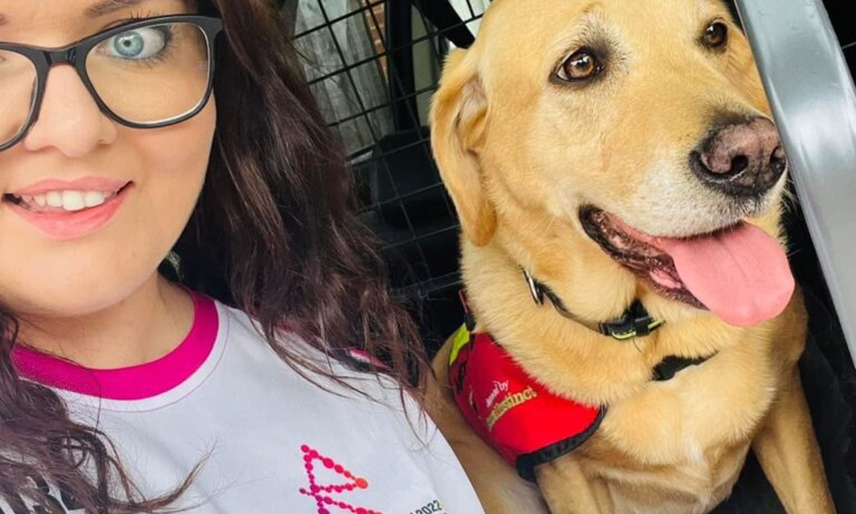 Emma Partlow, a white female and Transreport's Accessibility & Inclusion Manager, sitting beside her assistance dog Luna.