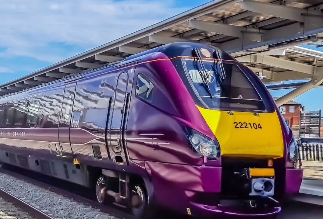 A purple and yellow East Midlands Railway train sat stationary at a train station.