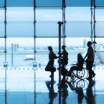 Blue-tinted photo of 4 people including a wheelchair user in the airport.