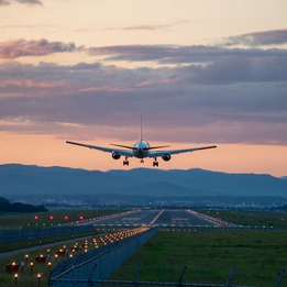 Photo of a plane above a runway at sunset.