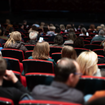 A photo of people at a venue seated in red chairs in the audience.