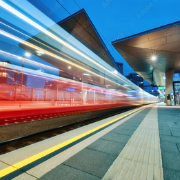 Photo of a red train speeding past a platform with a blur effect to convey movement.