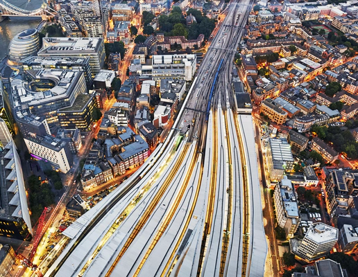 An aerial view of several trains on converging train tracks in a big city with skyscrapers.