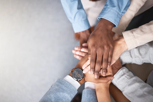 A group of diverse hands stacked together in a gesture of teamwork and unity.