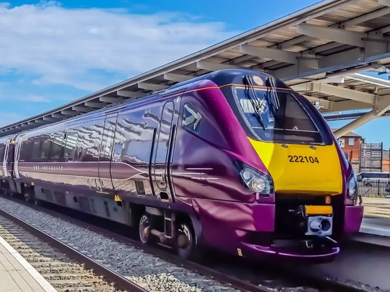 A purple and yellow East Midlands Railway train sat stationary at a train station.