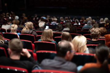 A photo of people at a venue seated in red chairs in the audience.