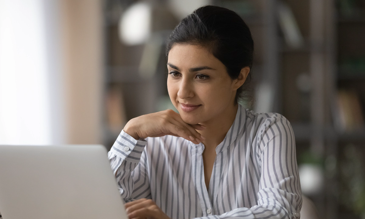 A woman in a blouse sitting in front of an open laptop computer.